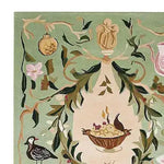 A beautifully detailed corner of the 'Ornaments and Offerings Hand Tufted Rug', showcasing an intricate design with a floral and bird motif on a light green wool background. This area rug is perfect for adding an artistic touch to large living rooms, enhancing the space with its elegant patterns and rich colors.