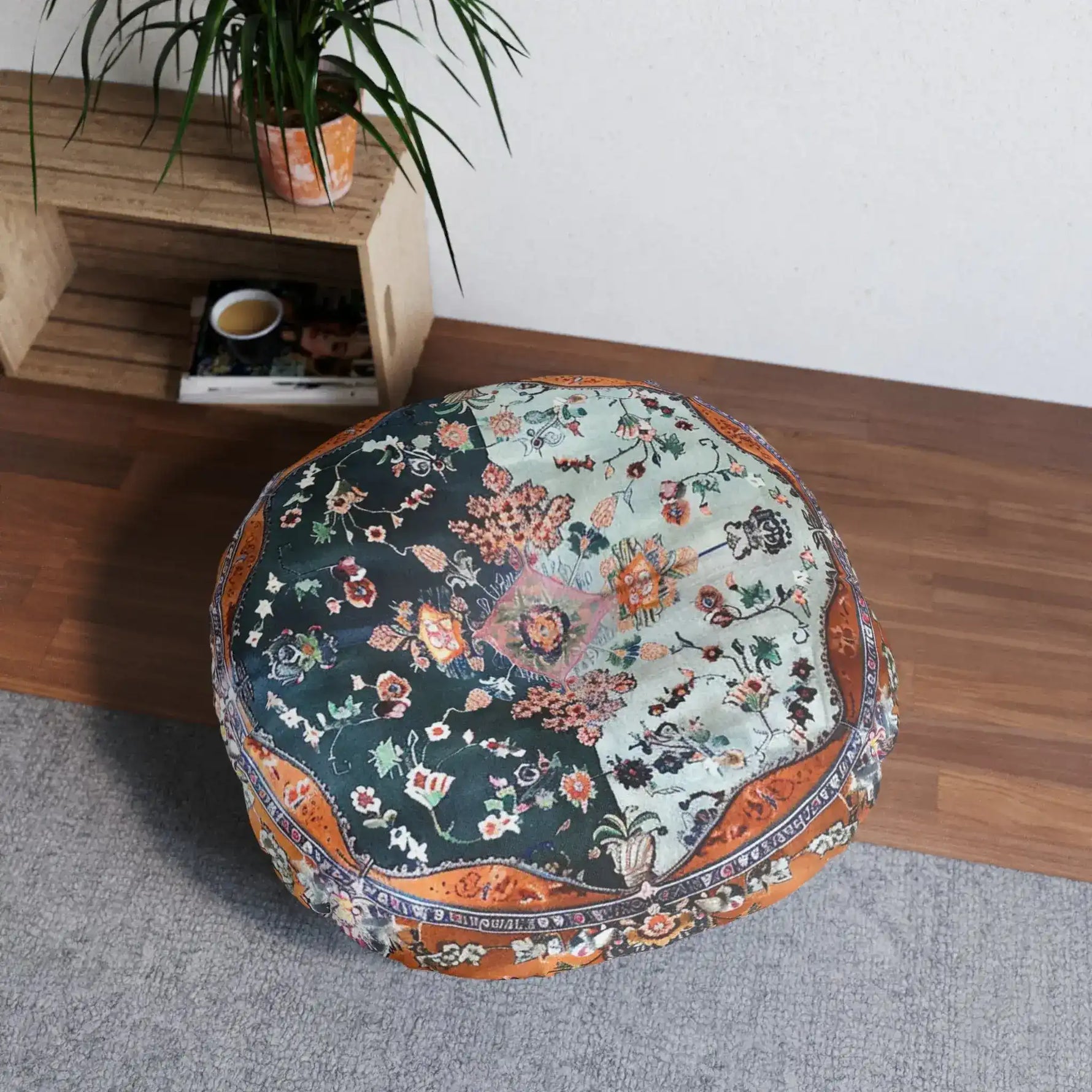 Ornate Floral and Geometric Floor Pillow with split dark-forest and light-sage floral print and copper border, shown beside a wooden shelf in a living space