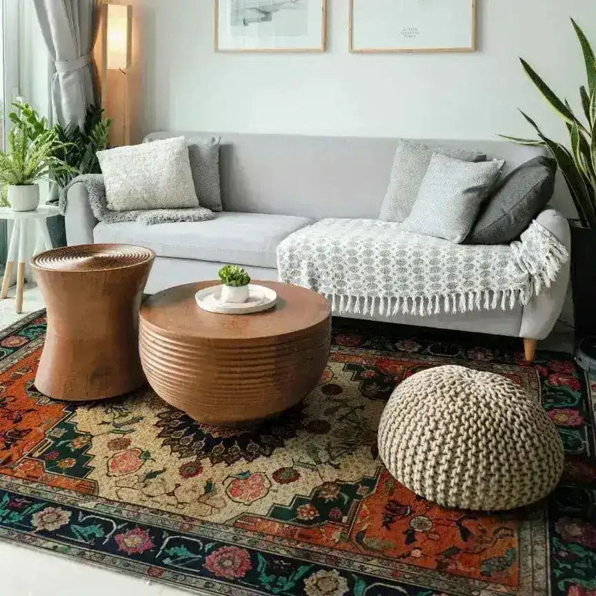 Cozy living room featuring an Ornate Floral Crest Hand Knotted Area Rug, showcasing vintage Persian rug patterns. The large area rug adds warmth and charm, complementing the modern decor with a comfortable grey sofa, wooden coffee tables, and lush greenery.