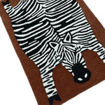 This image features an oversized zebra hand-tufted wool rug, perfect for adding a unique touch to your living room or dining room area. The rug showcases a detailed zebra design in black and white on a warm brown background, making it a striking piece for any space.