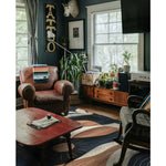 Cozy living room featuring a Palm Echoes Hand Tufted Rug, an elegant area rug with a contemporary design. The wool rug showcases a blend of vintage and modern styles, enhancing the room's decor with its artistic patterns. Surrounded by classic leather and wooden furniture, this area rug is perfect for living room or office spaces, adding warmth and style.