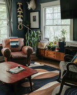 Cozy living room featuring a Palm Echoes Hand Tufted Rug, an elegant area rug with a contemporary design. The wool rug showcases a blend of vintage and modern styles, enhancing the room's decor with its artistic patterns. Surrounded by classic leather and wooden furniture, this area rug is perfect for living room or office spaces, adding warmth and style.