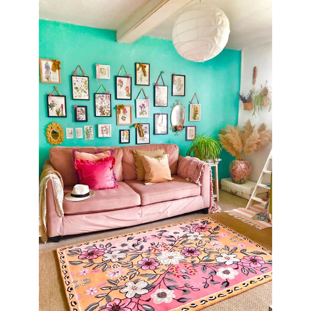 A cozy living room featuring a vibrant, hand-tufted wool area rug with a floral design. This vintage-style rug adds a touch of elegance and charm, perfect for enhancing the ambiance of living room spaces. The pastel-colored floral patterns on the rug complement the pink sofa and the eclectic gallery wall, creating a harmonious and inviting atmosphere.