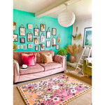 A vibrant living room showcasing a Pastel Paradise Hand Tufted Rug with a beautiful floral design. This area rug features pink and orange hues, perfect for adding a vintage touch to your living room. The wool rug complements the cozy pink sofa adorned with colorful cushions, creating an inviting and stylish space. Ideal for those seeking living room area rugs that combine elegance and comfort.