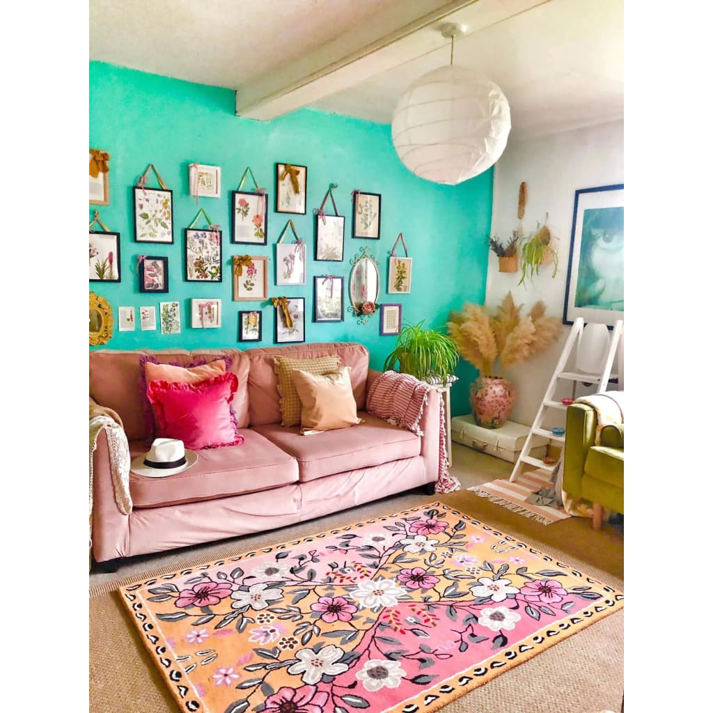A vibrant living room showcasing a Pastel Paradise Hand Tufted Rug with a beautiful floral design. This area rug features pink and orange hues, perfect for adding a vintage touch to your living room. The wool rug complements the cozy pink sofa adorned with colorful cushions, creating an inviting and stylish space. Ideal for those seeking living room area rugs that combine elegance and comfort.