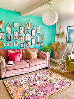 A vibrant living room showcasing a Pastel Paradise Hand Tufted Rug with a beautiful floral design. This area rug features pink and orange hues, perfect for adding a vintage touch to your living room. The wool rug complements the cozy pink sofa adorned with colorful cushions, creating an inviting and stylish space. Ideal for those seeking living room area rugs that combine elegance and comfort.