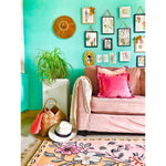 A vibrant living room featuring a pastel paradise hand tufted area rug with floral patterns. The wool rug complements the vintage decor, including a blush sofa with pink cushions, and a gallery wall of botanical prints. Ideal for those seeking stylish living room area rugs that add a touch of elegance and warmth.
