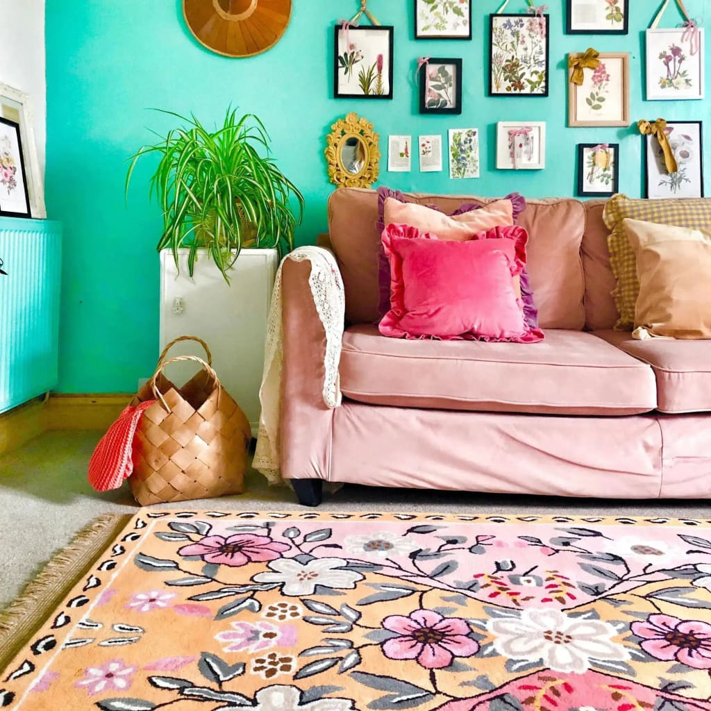 A cozy living room featuring a beautifully designed Pastel Paradise Hand Tufted Rug. This floral area rug, perfect for adding a vintage touch to living room spaces, showcases intricate flower patterns in soft pastel colors. The wool rug is set against a stylish pink sofa adorned with vibrant throw pillows, creating an inviting atmosphere. Ideal for those seeking elegant rugs for living room decor.