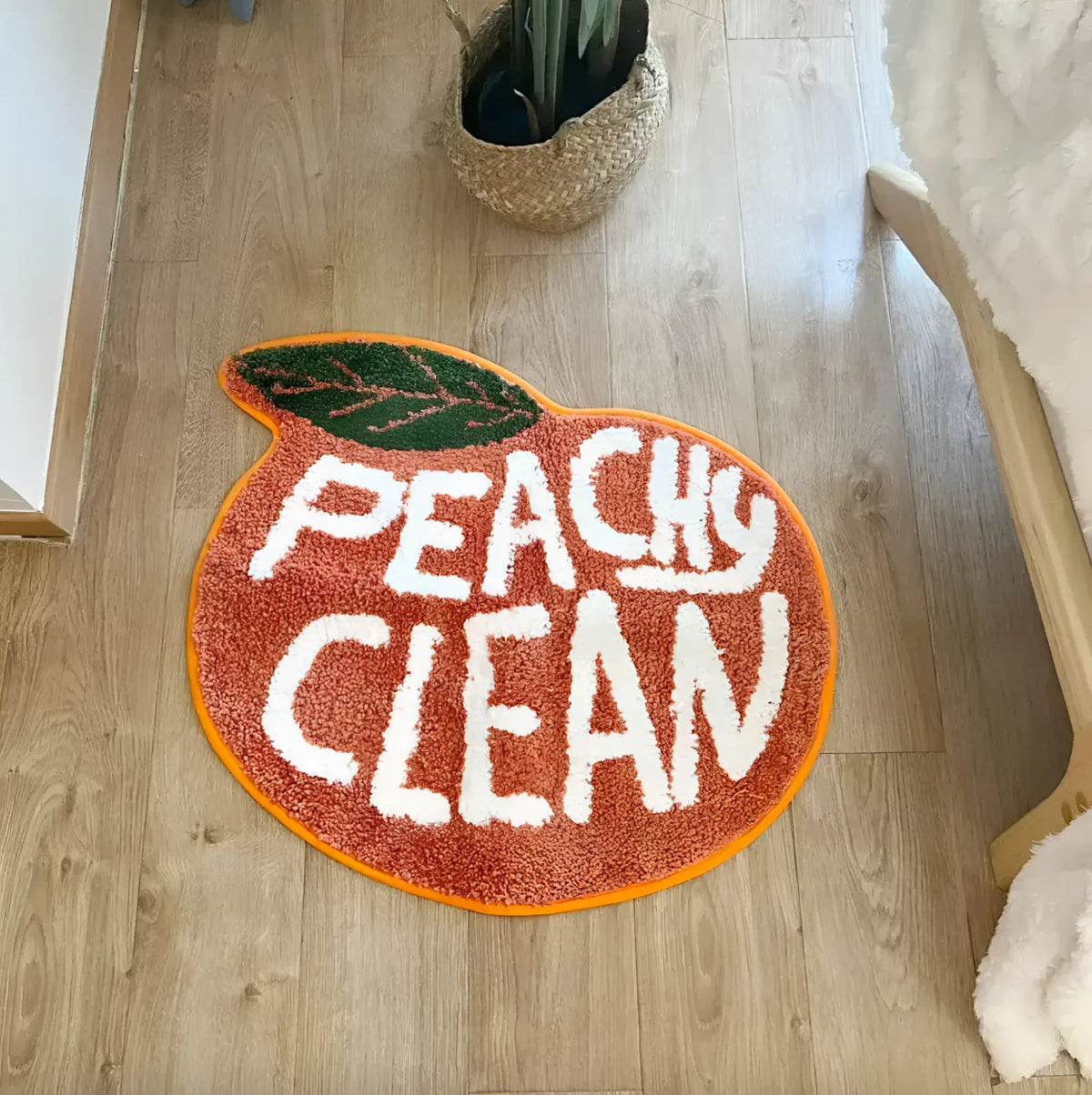 A vibrant peach-shaped bathmat with the words 'Peachy Clean' in bold white letters, perfect for adding a playful touch to your bathroom or kitchen. This cotton runner rug, ideal as a hallway runner rug or kitchen runner rug, is set against a warm wooden floor, offering a cozy and inviting atmosphere.
