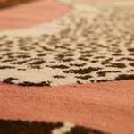 Close-up of a tufted wool rug with a leopard print pattern on a pink background