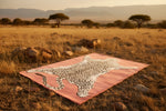 Leopard skin pattern on a pink rug in a savannah setting with trees and mountains.