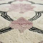 Close-up of a textured rug with pink floral patterns and black geometric lines.