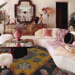 A stylish living room featuring a vibrant 'Petals in Motion' hand-knotted area rug with a vintage Persian design. The rug, with its intricate patterns and rich colors, complements a modern decor setting with plush pink cushions and elegant furnishings.