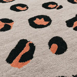 Close-up view of a pink and black leopard print hand-tufted wool area rug. The abstract design adds a vibrant touch, perfect for a large living room, hallway runner, or as a unique kitchen rug.