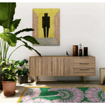 Stylish living room featuring a Pink Gingko Leaves Hand Tufted Wool Rug on a wooden floor. The vibrant area rug, suitable for large living rooms, adds a pop of color with its pink and green floral design. A mid-century modern wooden sideboard stands against the wall, adorned with decorative vases. A large plant adds a touch of nature, complementing the cozy ambiance of this living room. Perfect choice for those looking for living room rugs 8x10.