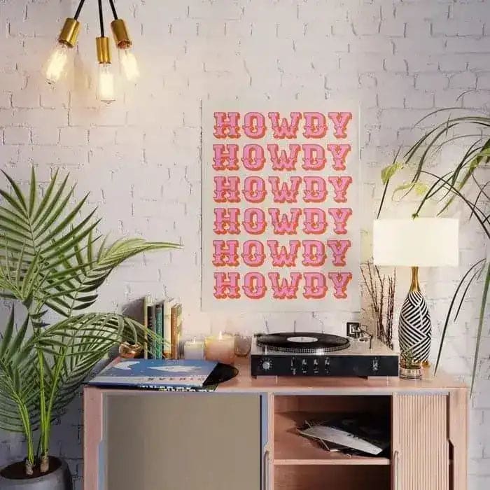 Stylish room featuring a Pink Howdy Wall Art Poster on a white brick wall, beautifully complementing a cozy, modern setup. The setting includes a wooden console with a record player, books, and a chic lamp, all adding a warm touch to a space perfect for showcasing area rugs. Ideal for those seeking living room area rugs or large living room rugs to enhance their decor.