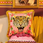Vibrant pink throw pillow featuring a fierce leopard face design surrounded by floral accents, complemented by a luxurious gold fringe.