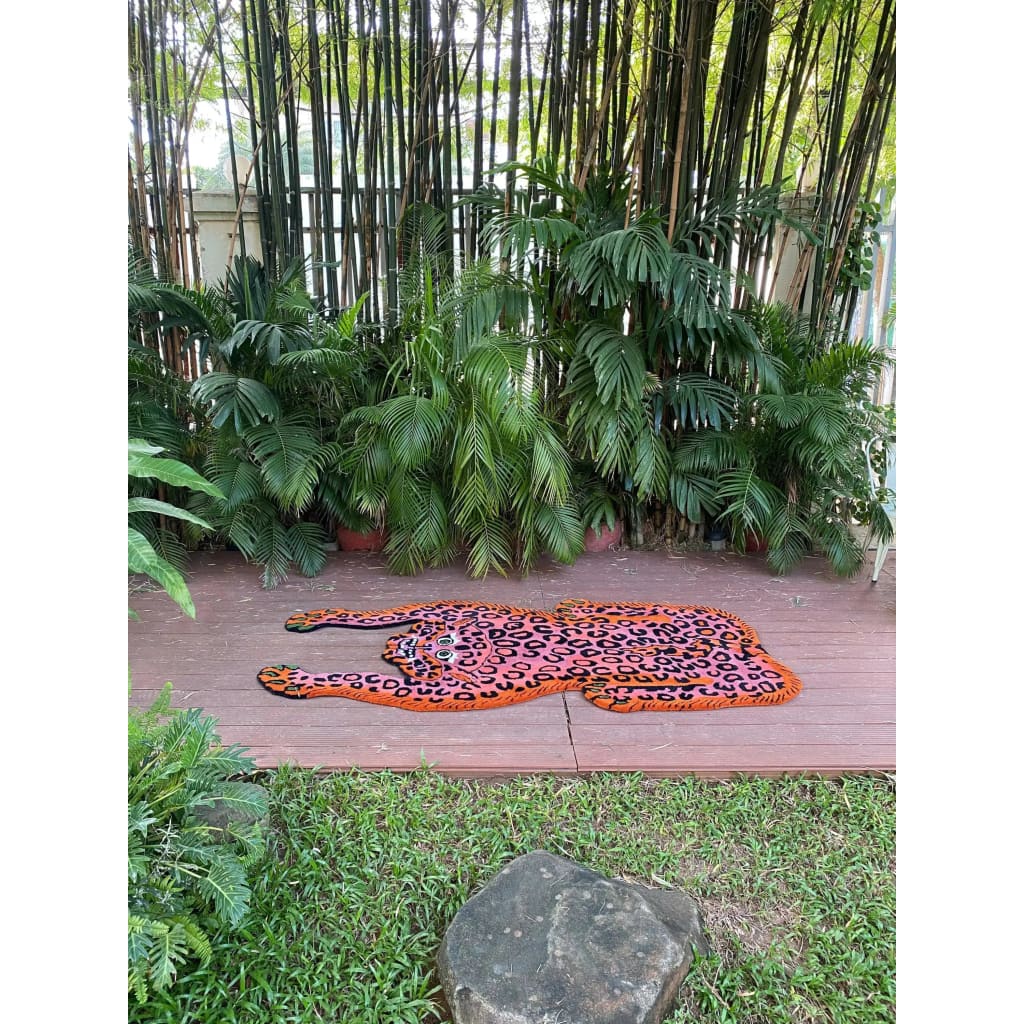 Vibrant pink leopard yogi accent wool rug displayed outdoors on a wooden deck, surrounded by lush green plants, showcasing its unique and artistic design. Ideal for adding a pop of color to living room spaces. Perfect as a living room rug 8x10, this vintage wool rug adds a bold touch to any area.