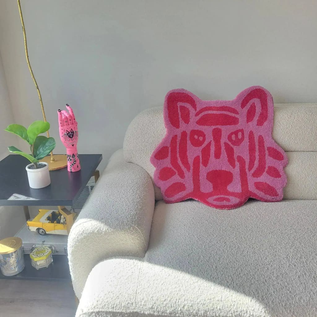 A vibrant pink lion face hand-tufted wool area rug displayed on a cozy cream couch, perfect for adding a pop of color to office spaces. This round rug, ideal for rugs for office, showcases intricate tufting details, enhancing the decor with its unique design.