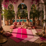 Woman sitting on a colorful rug in a luxurious outdoor setting with plants and a pool.
