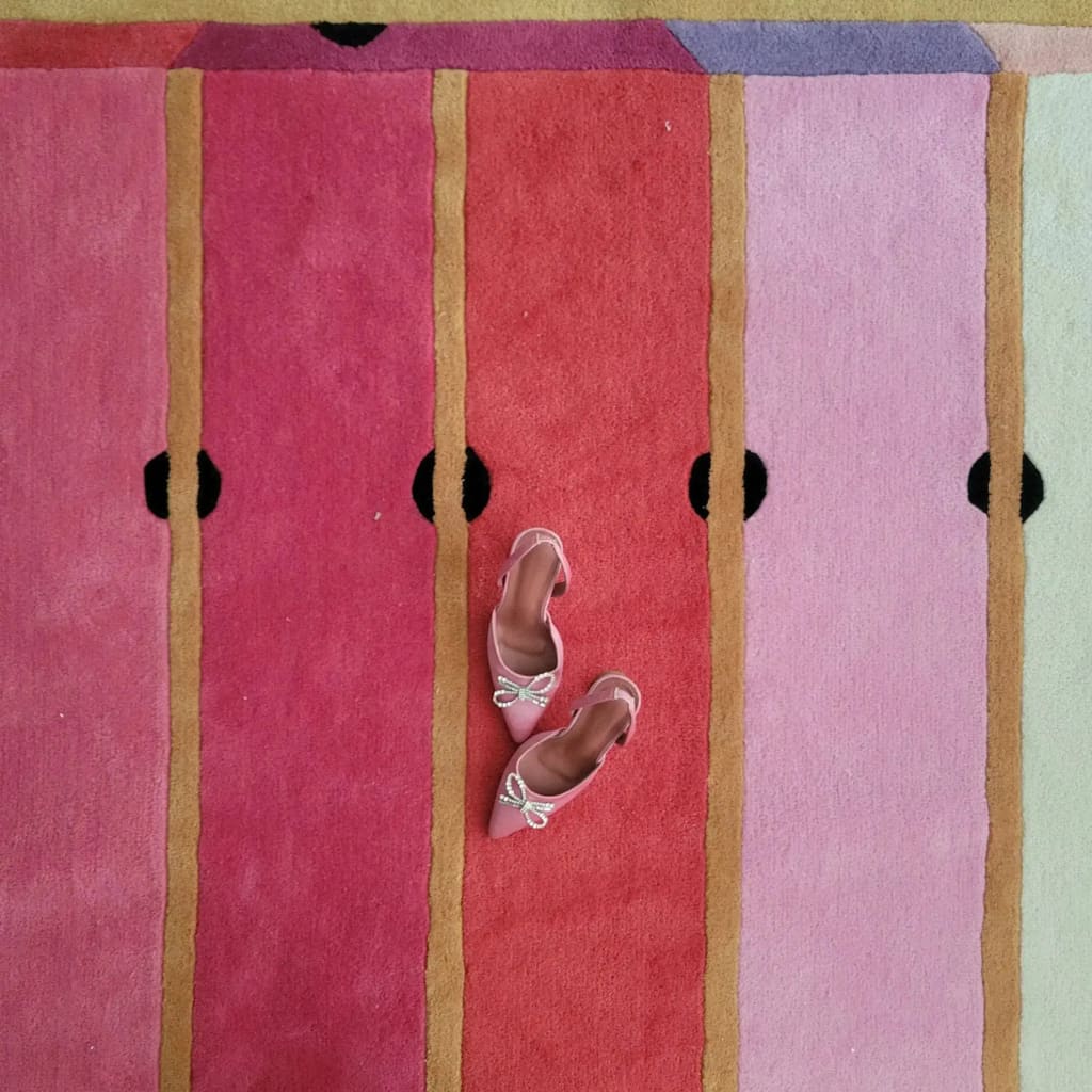 A vibrant Pink Prism Geometric Hand-Tufted Wool Rug displayed with a pair of stylish pink shoes on top. This contemporary rug features bold, colorful stripes, perfect for adding a modern touch to any living room. Ideal for those seeking unique area rugs for living room spaces, this wool rug combines vintage charm with contemporary design.