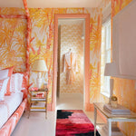 Pink, red, and black abstract brushstroke wool runner in a tropical-wallpapered bedroom with a side table and lamp