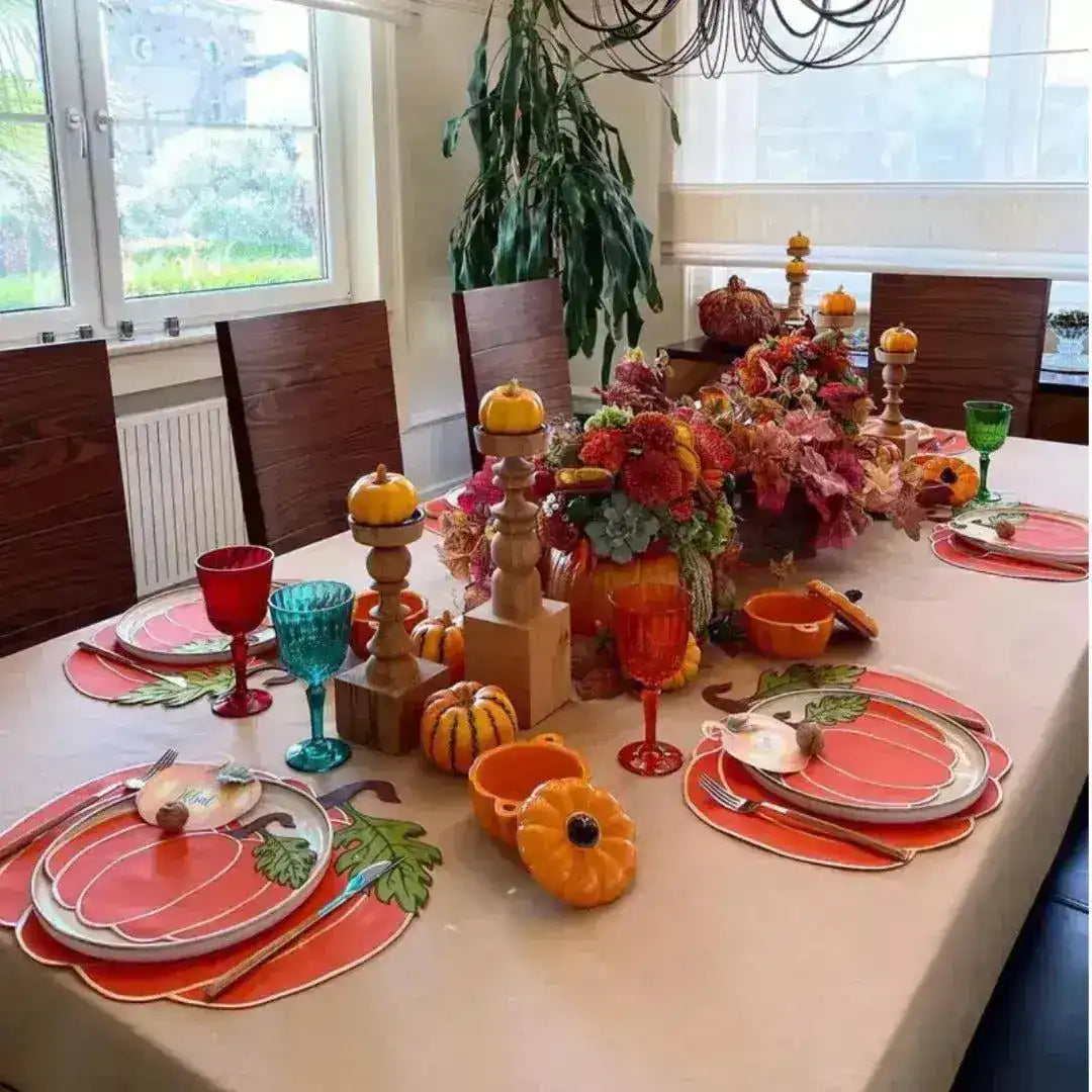 Autumn dining table with pumpkin-shaped placemats, pumpkin-print plates, orange candle holders and fall florals