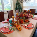 Autumn dining table with pumpkin-shaped placemats, pumpkin-print plates, orange candle holders and fall florals