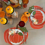 Overhead view of two pumpkin-shaped placemats with green leaf tail embroidery, pumpkin china and ceramic accents