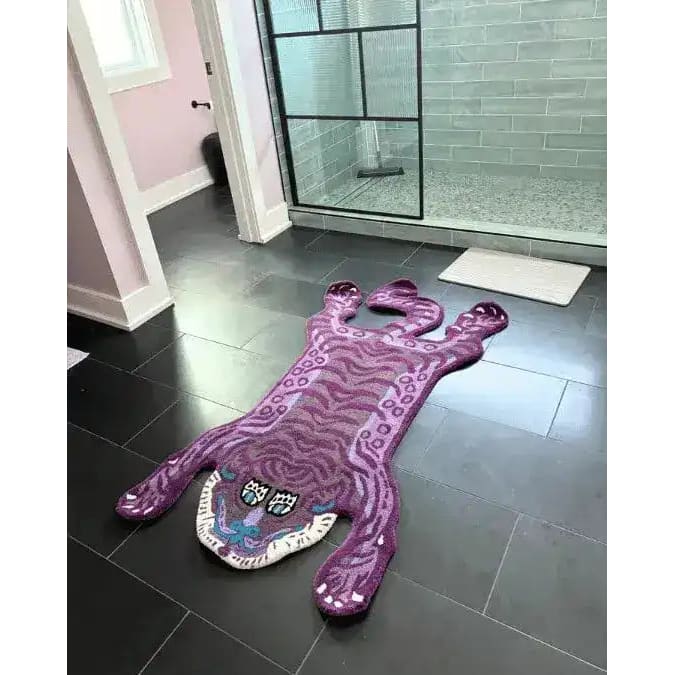 A striking Purple Tibetan Tiger Accent Hand Tufted Wool Rug laid out in a modern bathroom with dark tiles. This unique area rug, designed in the shape of a tiger, adds a vintage touch to large living rooms or any space needing a bold accent. Perfect for those seeking large area rugs or wool rugs to enhance their living room decor.