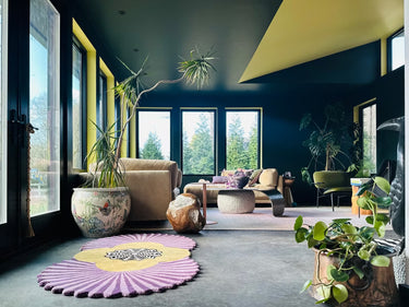 Modern living room with a purple rug, beige sofa, and large windows.