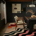 A stylish dining room featuring a Radiant Harmony Hand Tufted Rug. This contemporary area rug, perfect for both living room and dining room spaces, showcases an abstract design with flowing waves of color, enhancing the modern decor. The wool rug adds warmth and texture, complementing the elegant wooden chairs and dark walls.