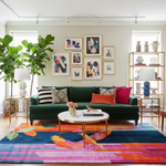 Modern living room with a green sofa, colorful rug, and decorative wall art.