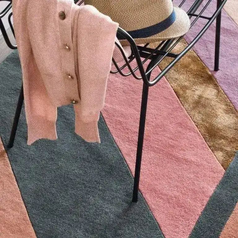 A stylish living room showcasing a Rainbow Geometry Retro Hand Tufted Wool Rug. The area rug features a vibrant mix of geometric patterns in pink, green, and brown tones, perfect for adding a vintage touch to any bedroom or living room. An elegant chair with a pink sweater and straw hat complements the cozy setting, ideal for spaces needing an 8x10 wool rug.