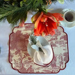 red and cream placemats overhead view with toile print, white napkin and butterfly ring, orange amaryllis and pine greenery