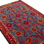 A vibrant Red Bloom Harmony hand-tufted wool area rug, perfect for adding a floral and vintage touch to your dining room or living room. The rug features an intricate design with red and orange flowers against a blue background, ideal for 8x10 living room settings.