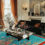 A beautifully decorated living room featuring a vibrant 'Red Bordered Spring Floral in the Blue Sky' wool hand-knotted area rug. The large living room rug adds a splash of color with its floral design, complementing the elegant decor and cozy seating arrangement.