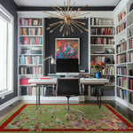 A beautifully styled home office features a hand-knotted area rug with a vibrant red border and intricate spring floral design on a green background. This living room area rug adds a touch of elegance and color to the modern space, blending seamlessly with the bookshelf-lined walls and sleek desk setup.