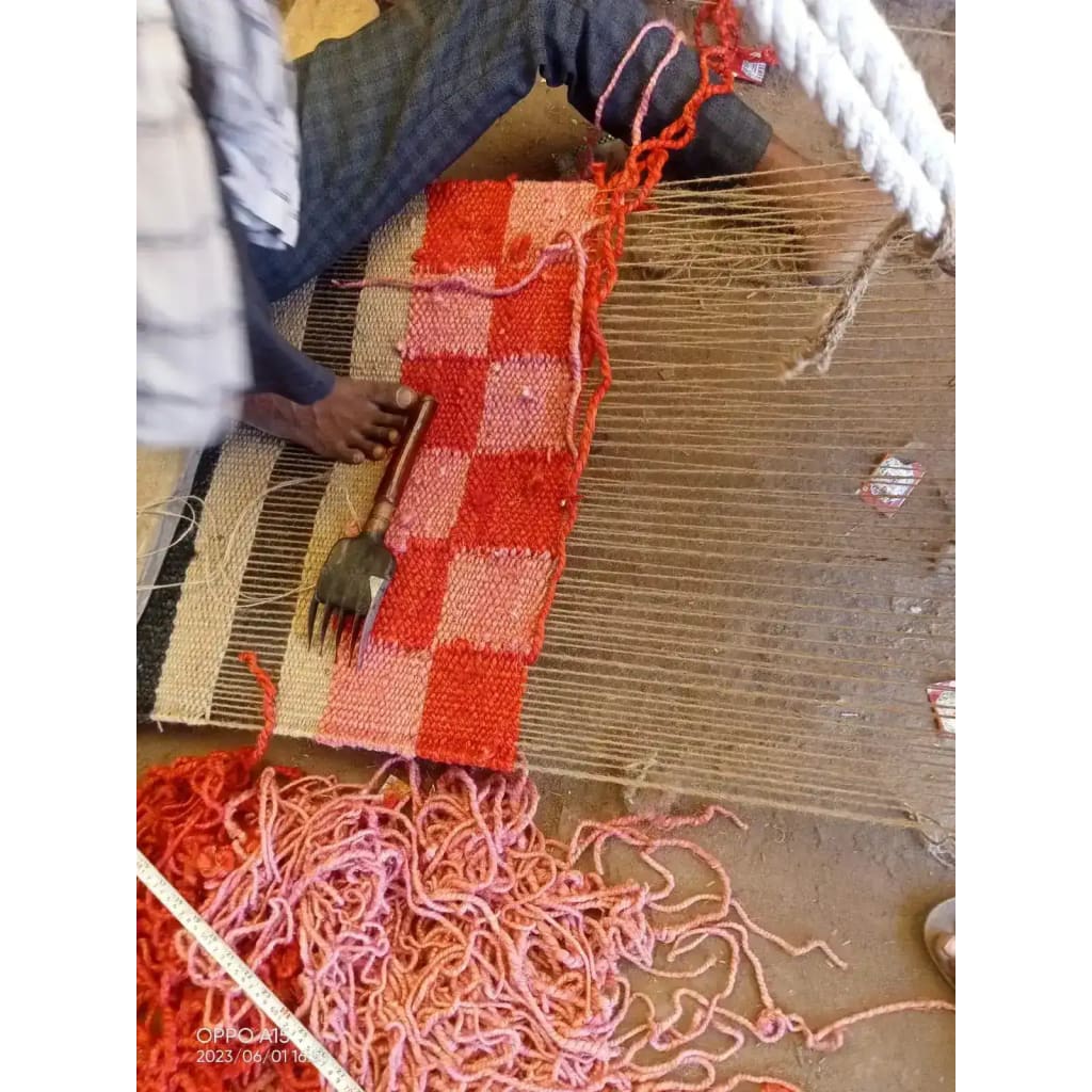 A craftsman weaving a red checker jute area rug, showcasing intricate handmade detail. Ideal for adding a vibrant touch to an office or as a large area rug for a living room.