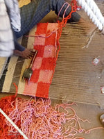 A craftsman weaving a red checker jute area rug, showcasing intricate handmade detail. Ideal for adding a vibrant touch to an office or as a large area rug for a living room.
