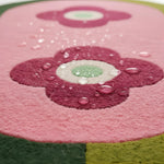 Close-up of a pink flower-shaped rug with water droplets on a pink background