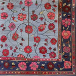 A detailed view of the Red Velvet Bloom Hand Knotted Area Rug, showcasing its intricate floral design. Perfect for adding a touch of elegance to any living room, this 8x10 vintage rug features vibrant red and pink blossoms on a classic Persian-style background.