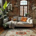 A cozy living room featuring a Regal Blossom Medallion Hand Knotted Area Rug with a vintage Persian design. The large rug showcases intricate floral patterns in vibrant colors, perfectly complementing the rustic brick wall and modern gray sofa adorned with colorful cushions. Ideal for adding elegance to large living rooms.