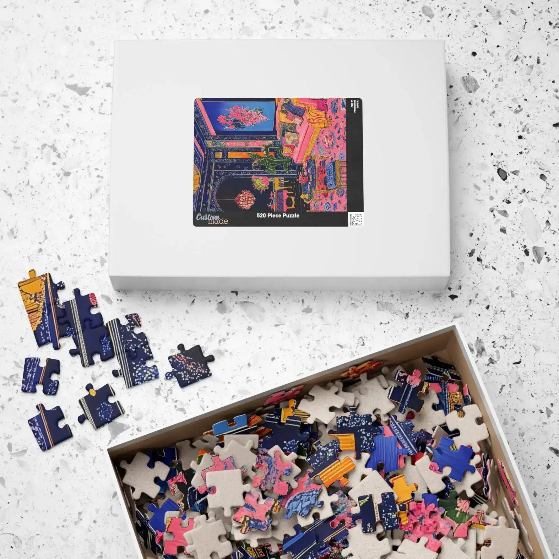 Overhead flat-lay of Regal Eclectic Puzzle white 520-piece box beside open tray overflowing with loose colorful pieces on terrazzo
