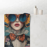 Renaissance Butterfly in Couture bath towel draped over bathtub in white bathroom, bold orange wings and blue sunglasses print