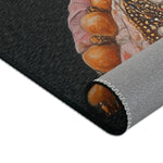 Corner of Renaissance Rooster Couture Rug folded on dark ground, wooden bead necklace detail visible at rolled edge, grey non-slip backing showing