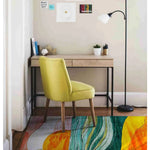 A vibrant Retro Seaside Oasis Hand Tufted Area Rug displayed in a cozy bedroom setting. This contemporary rug, made of high-quality wool, adds a splash of color with its abstract design featuring waves of green, yellow, and orange. Positioned under a stylish yellow chair and a minimalist desk, it enhances the modern aesthetic of the room, making it ideal for both bedroom and office spaces.