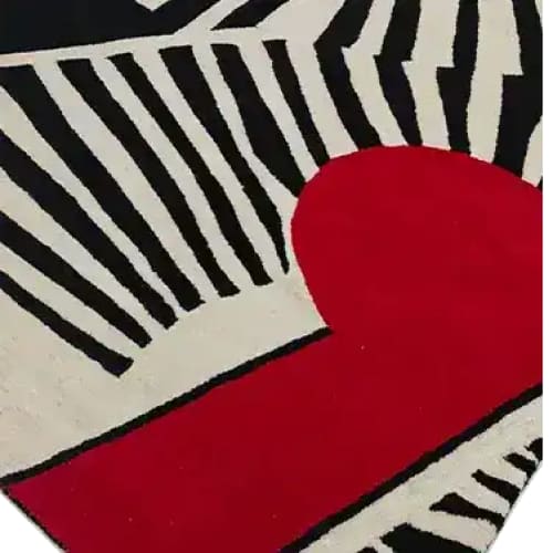 Close-up of the Rhythmic Rays Hand Tufted Area Rug showcasing its bold abstract design in black and white stripes with a striking red accent. Ideal for enhancing the aesthetic of living room and dining room spaces, this wool rug offers a modern touch.