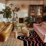 A cozy office space featuring the Rippling Rhapsody Hand Tufted Viscose Area Rug. This contemporary rug, with its abstract wave design in black, pink, and beige, adds a stylish touch to the room. It complements the elegant velvet couches and glass coffee table, creating an inviting atmosphere ideal for a sophisticated office setting.