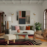 A stylish contemporary area rug with swirling patterns in black, pink, and orange hues, enhancing a modern office setting. The rug is placed under a chic glass-top coffee table, surrounded by a white sofa, colorful cushions, and elegant decor, making it an ideal wool rug for office spaces.